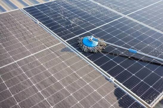 Dusty ground-mounted solar panels being cleaned with a soft mop, showing the dirty surface next to freshly cleaned glass